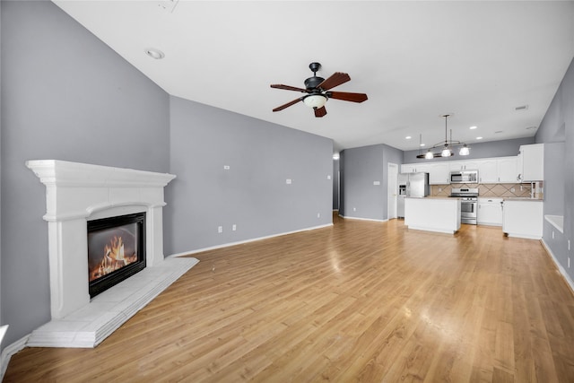 unfurnished living room featuring baseboards, ceiling fan, light wood-style floors, and a glass covered fireplace