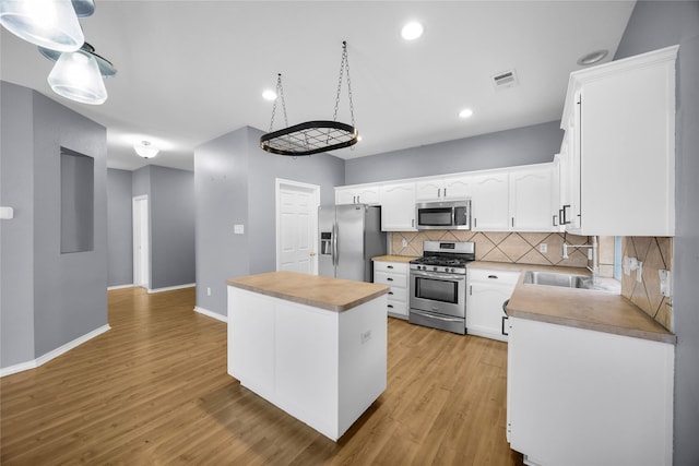 kitchen with a sink, light wood-type flooring, visible vents, backsplash, and appliances with stainless steel finishes