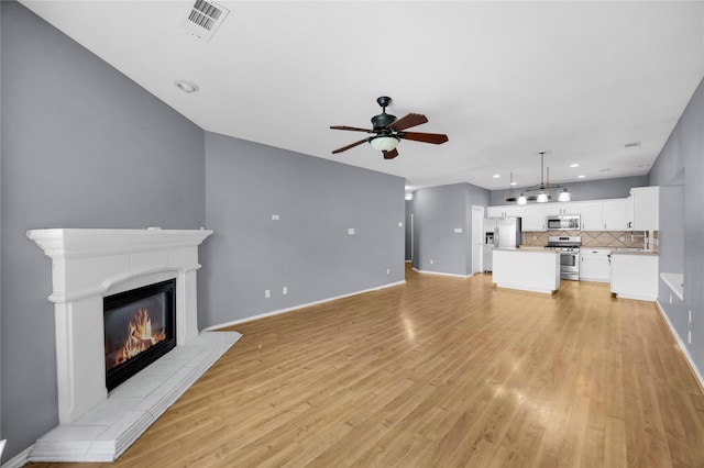 unfurnished living room with light wood-style floors, ceiling fan, a glass covered fireplace, visible vents, and baseboards