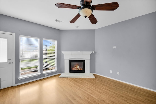 unfurnished living room with visible vents, baseboards, wood finished floors, and a glass covered fireplace