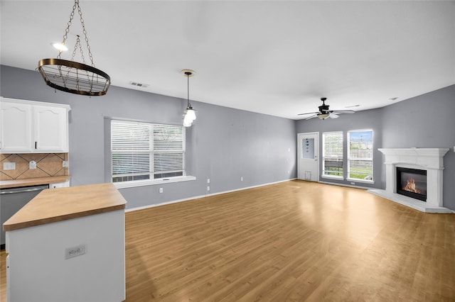 unfurnished living room with a glass covered fireplace, light wood-type flooring, a ceiling fan, visible vents, and baseboards