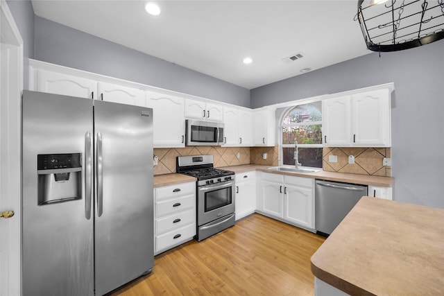 kitchen featuring white cabinets, a sink, visible vents, stainless steel appliances, and light wood finished floors