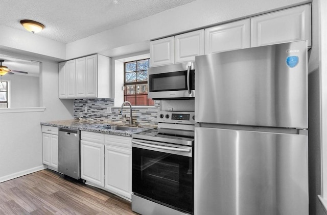 5316 Columbia Ave, Dallas, TX 75214 - kitchen featuring a sink, stainless steel appliances, tasteful backsplash, white cabinets, and wood finished floors