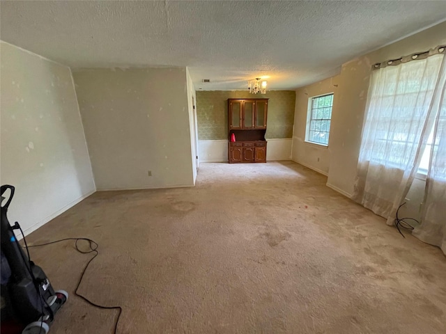 unfurnished living room featuring an inviting chandelier, a textured ceiling, baseboards, and light carpet