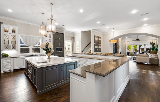 kitchen featuring a sink, a spacious island, visible vents, arched walkways, and gray cabinets