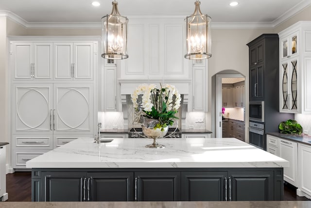 kitchen featuring arched walkways, a kitchen island with sink, oven, white cabinetry, and built in microwave