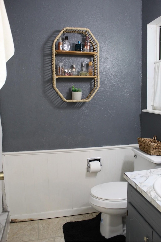 bathroom featuring a wainscoted wall, toilet, and vanity