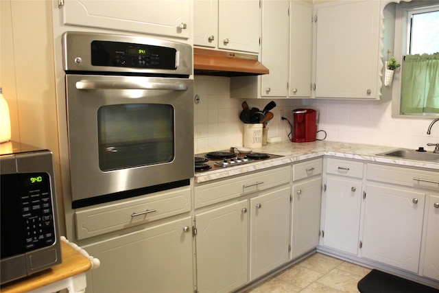 kitchen featuring tasteful backsplash, stainless steel appliances, under cabinet range hood, light countertops, and a sink