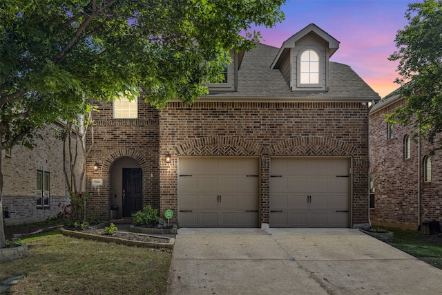 traditional home featuring a shingled roof, an attached garage, driveway, and brick siding