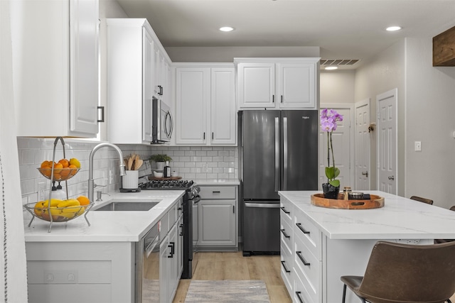 kitchen featuring visible vents, a sink, light stone counters, light wood-style floors, and stainless steel appliances