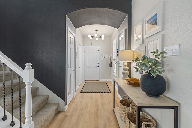 entryway featuring arched walkways, stairway, baseboards, a notable chandelier, and light wood-style flooring