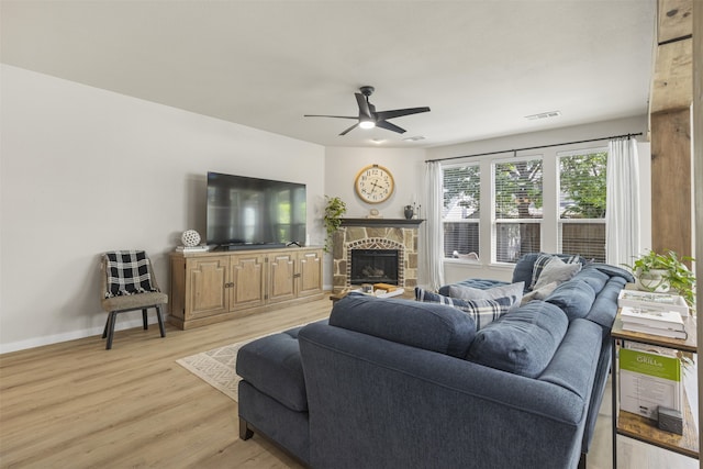 living area featuring ceiling fan, a stone fireplace, visible vents, baseboards, and light wood-style flooring