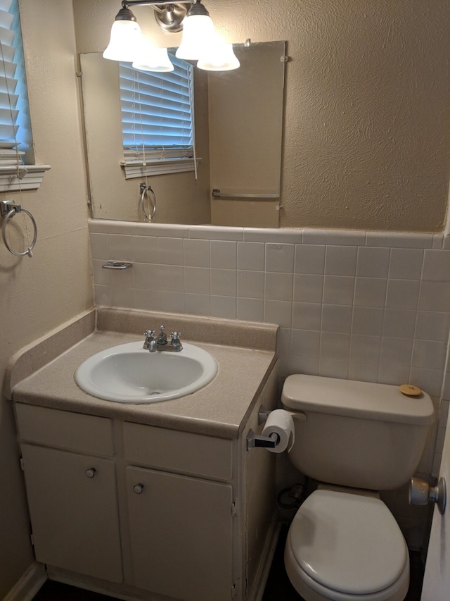 bathroom with toilet, tile walls, wainscoting, and vanity