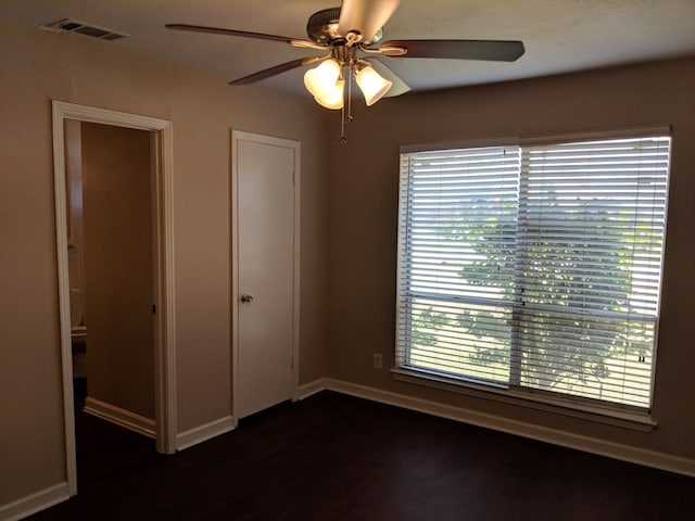 empty room featuring visible vents, ceiling fan, a healthy amount of sunlight, and dark wood finished floors