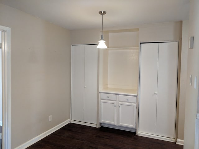 unfurnished dining area with dark wood-style flooring and baseboards