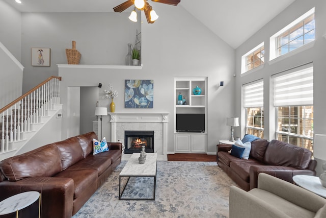 living room featuring a tile fireplace, high vaulted ceiling, ceiling fan, stairs, and wood finished floors