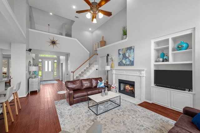 living area with ceiling fan, baseboards, a tile fireplace, wood finished floors, and high vaulted ceiling