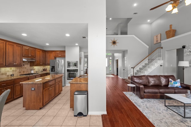 kitchen featuring a sink, stainless steel appliances, under cabinet range hood, stone countertops, and open floor plan