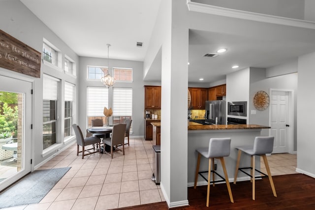 kitchen with brown cabinetry, a wealth of natural light, appliances with stainless steel finishes, and a chandelier
