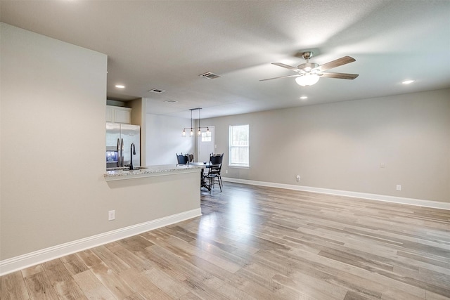 unfurnished living room featuring visible vents, a ceiling fan, light wood finished floors, and baseboards