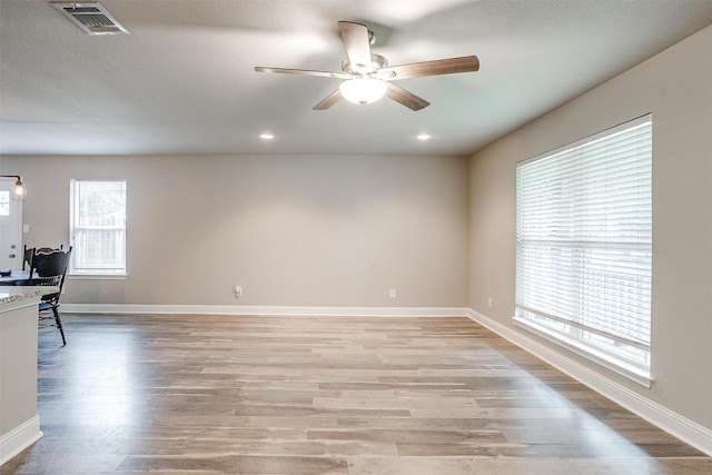 empty room with light wood finished floors, a ceiling fan, visible vents, and baseboards