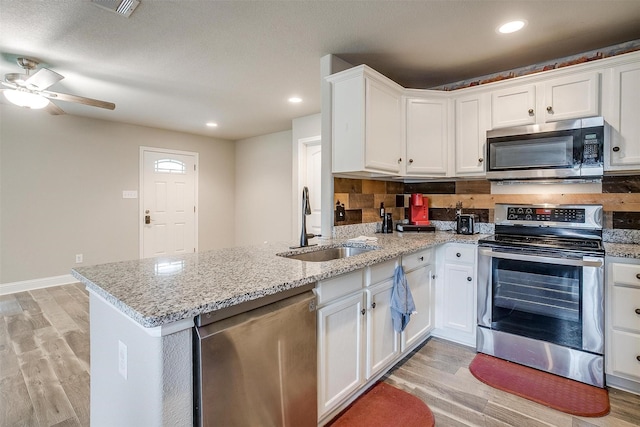 kitchen with a sink, stainless steel appliances, light wood-type flooring, white cabinetry, and a peninsula