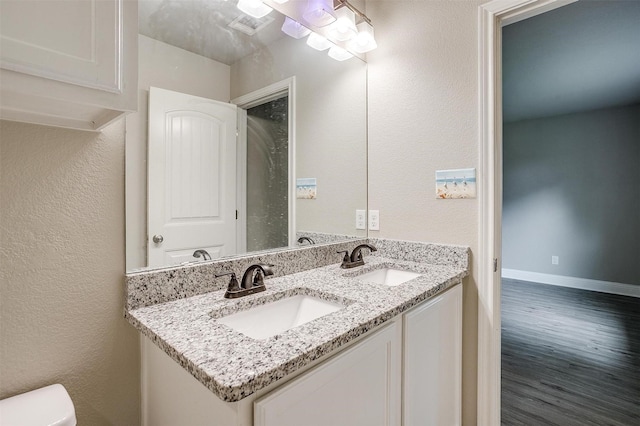 bathroom featuring toilet, double vanity, a sink, and wood finished floors
