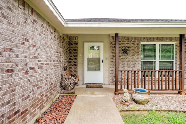 entrance to property with roof with shingles, covered porch, and brick siding