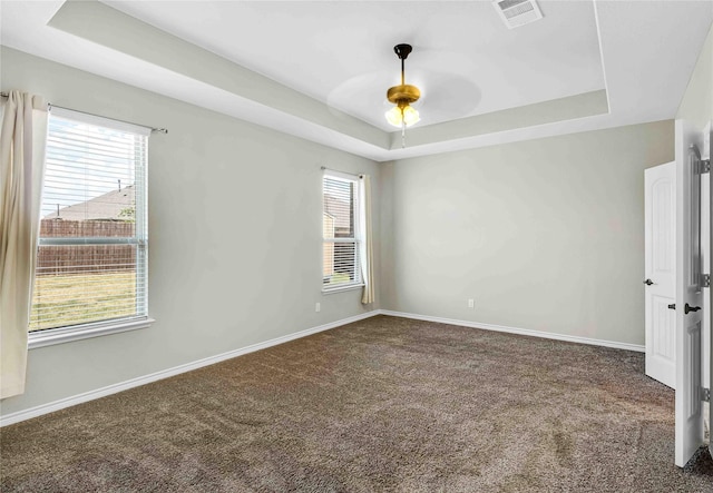 carpeted empty room featuring visible vents, a ceiling fan, a tray ceiling, and baseboards