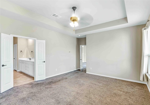 unfurnished bedroom with a sink, a tray ceiling, visible vents, light carpet, and baseboards