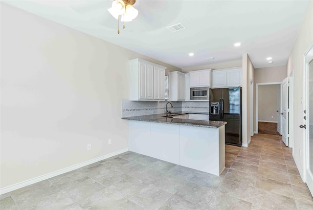kitchen with stainless steel microwave, black fridge with ice dispenser, backsplash, a sink, and baseboards