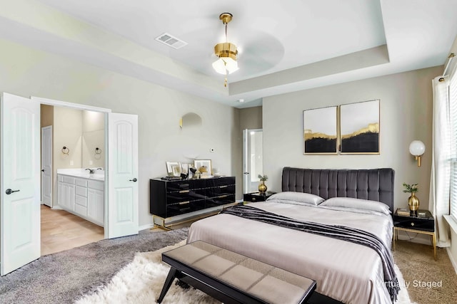 bedroom with a sink, visible vents, a tray ceiling, and light carpet