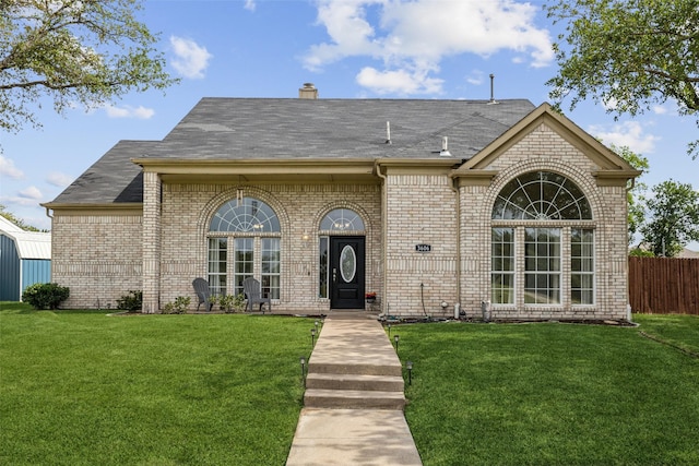 french provincial home with a chimney, a front yard, brick siding, and a shingled roof