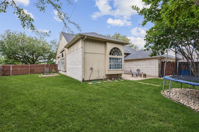 rear view of property with a yard, a patio area, a trampoline, and a fenced backyard