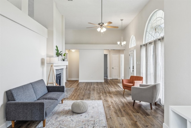 living room with wood finished floors, ceiling fan, a premium fireplace, a high ceiling, and baseboards