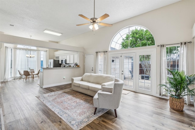 living room featuring a textured ceiling, ceiling fan with notable chandelier, french doors, and wood finished floors
