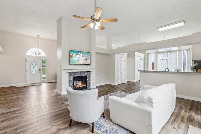living area with ceiling fan with notable chandelier, baseboards, a tiled fireplace, and wood finished floors