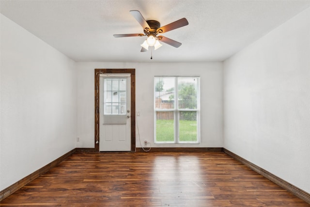 spare room with dark wood-type flooring, a ceiling fan, and baseboards