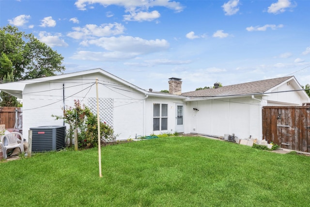 back of property featuring central AC unit, fence, a yard, and a chimney