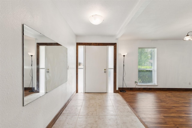 foyer featuring baseboards, a textured wall, and light tile patterned floors