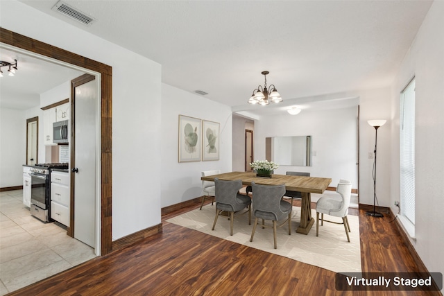 dining area featuring visible vents, light wood-style flooring, baseboards, and a notable chandelier
