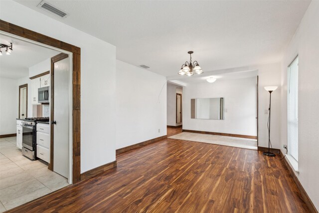 spare room featuring a chandelier, baseboards, visible vents, and light wood-type flooring