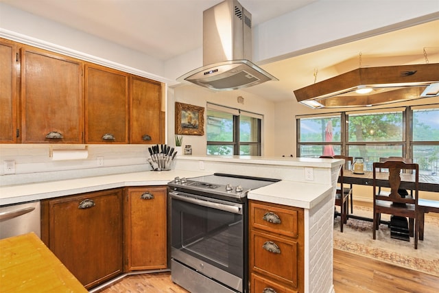 kitchen with island exhaust hood, stainless steel electric range oven, light wood-style flooring, a peninsula, and light countertops