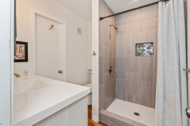 full bathroom featuring tiled shower, vanity, toilet, visible vents, and wood finished floors