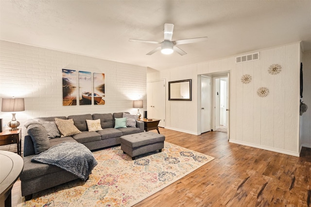 living room with visible vents, baseboards, brick wall, wood finished floors, and a ceiling fan