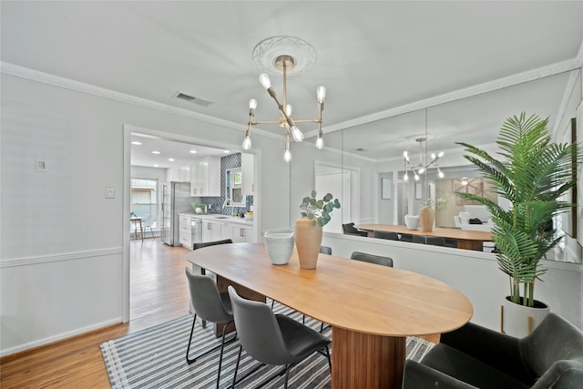 dining space with crown molding, visible vents, baseboards, light wood finished floors, and a notable chandelier