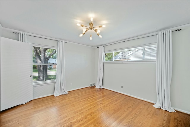 empty room with light wood finished floors, an inviting chandelier, baseboards, and visible vents