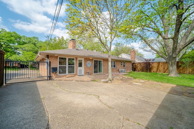 back of property with a chimney, a gate, brick siding, fence, and a lawn