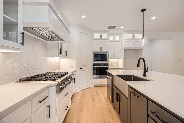 16090 Inca Dove Ct, Frisco, TX 75035 - kitchen with stainless steel appliances, custom exhaust hood, light wood-style flooring, white cabinets, and a sink