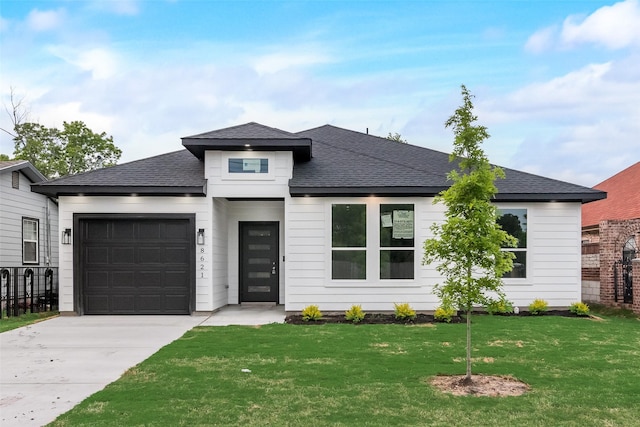 prairie-style house featuring a front lawn, fence, roof with shingles, an attached garage, and driveway